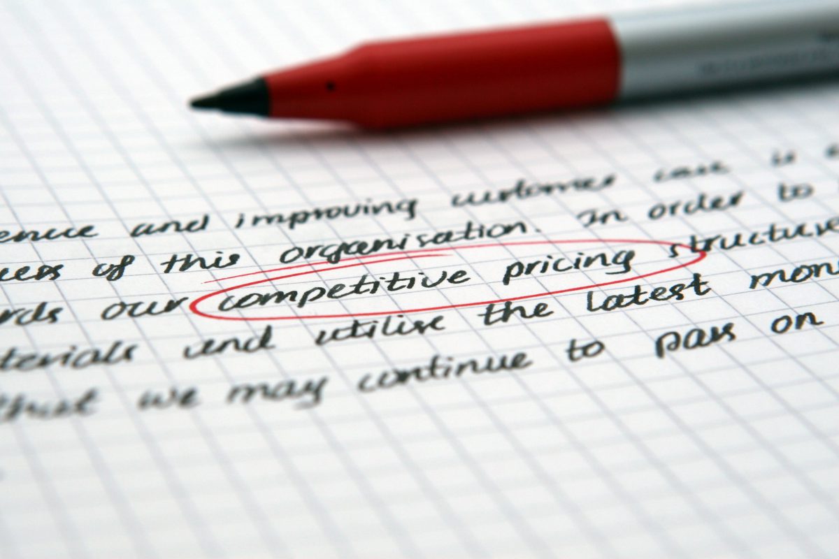 A close-up of writing with a pen next to it and the words competitive pricing highlighted