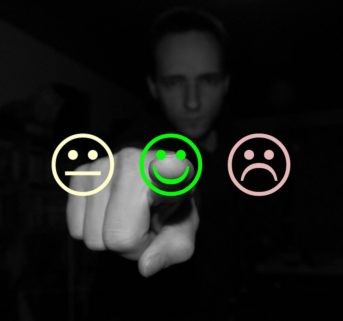 A Person pointing at a smiley face next to a sad face and neutral face