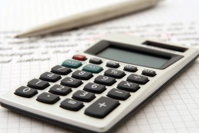A calculator laying on a sheet of graph paper with a ben behind it