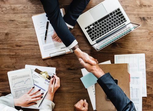 People shaking hands across a laptop and files.