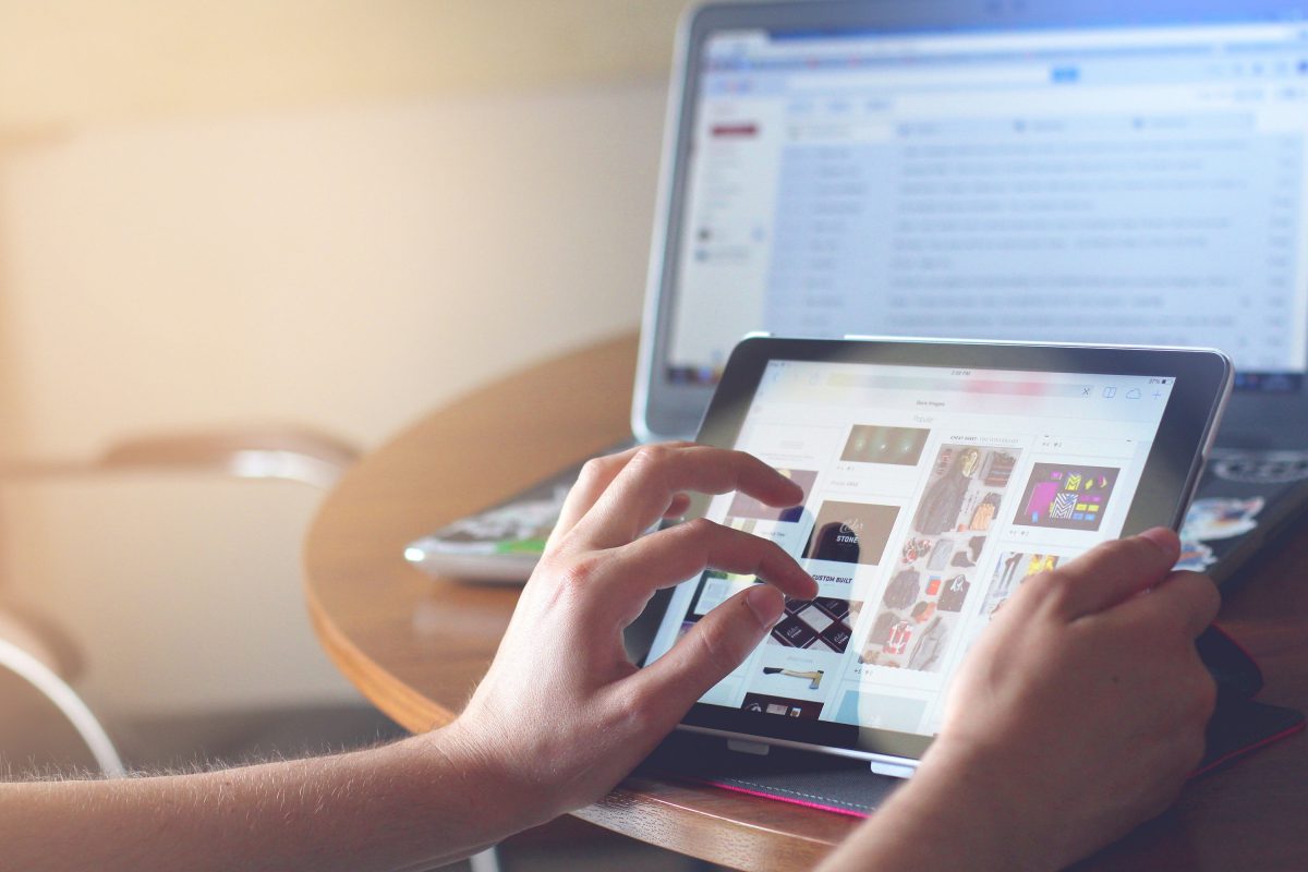 Person browsing on a tablet device with a laptop in the background.