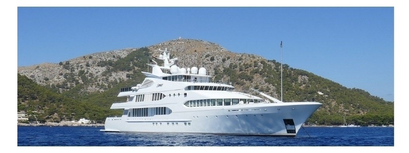 A large private yacht on the water in front of a mountain