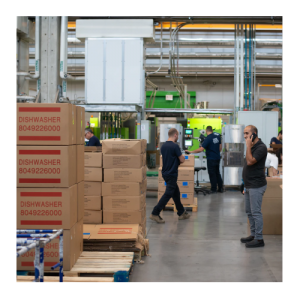 People working in a warehouse with a number of pallets of boxes visible