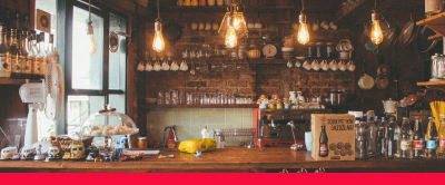 An image of a bar with bottles on it and mugs hanging from the wall behind it