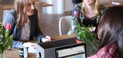 People chatting and meeting around a table with software displayed on a laptop