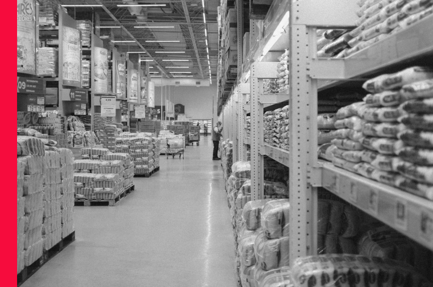 The view along the front of a section of racking in a store with a number of pallets of products next to it