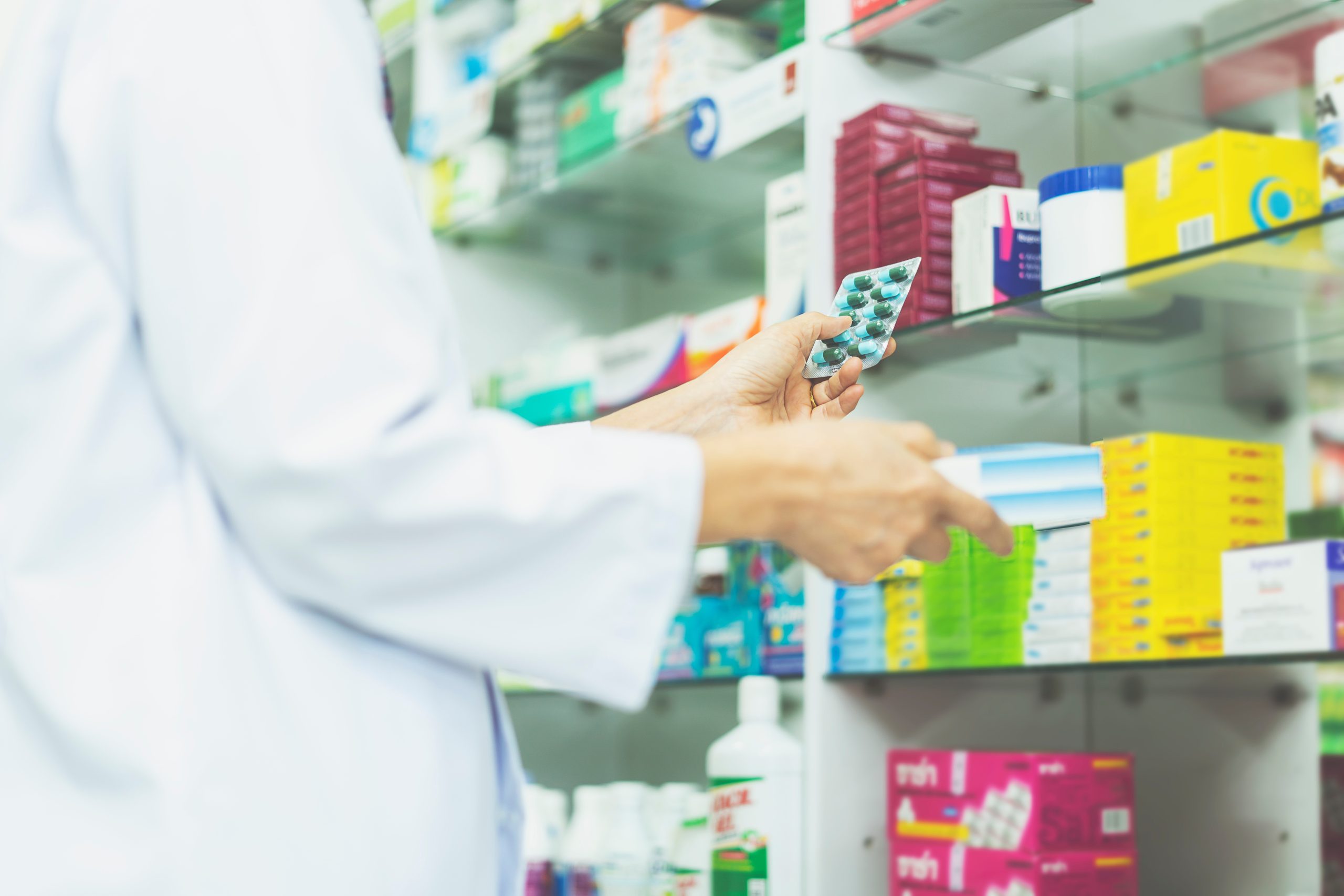 close up hand of Pharmacist holding medicine box and capsule pack in pharmacy drugstore. medicine, pharmaceutics, health care and people concept