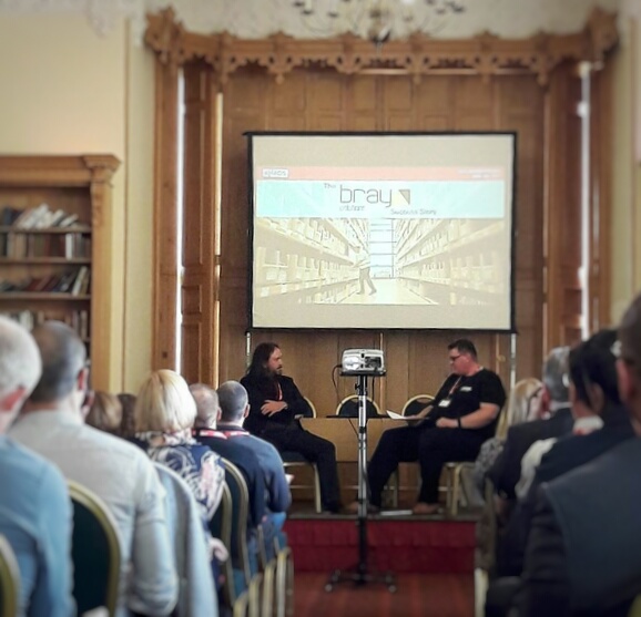 A audience of people watching two people on stage having a discussion