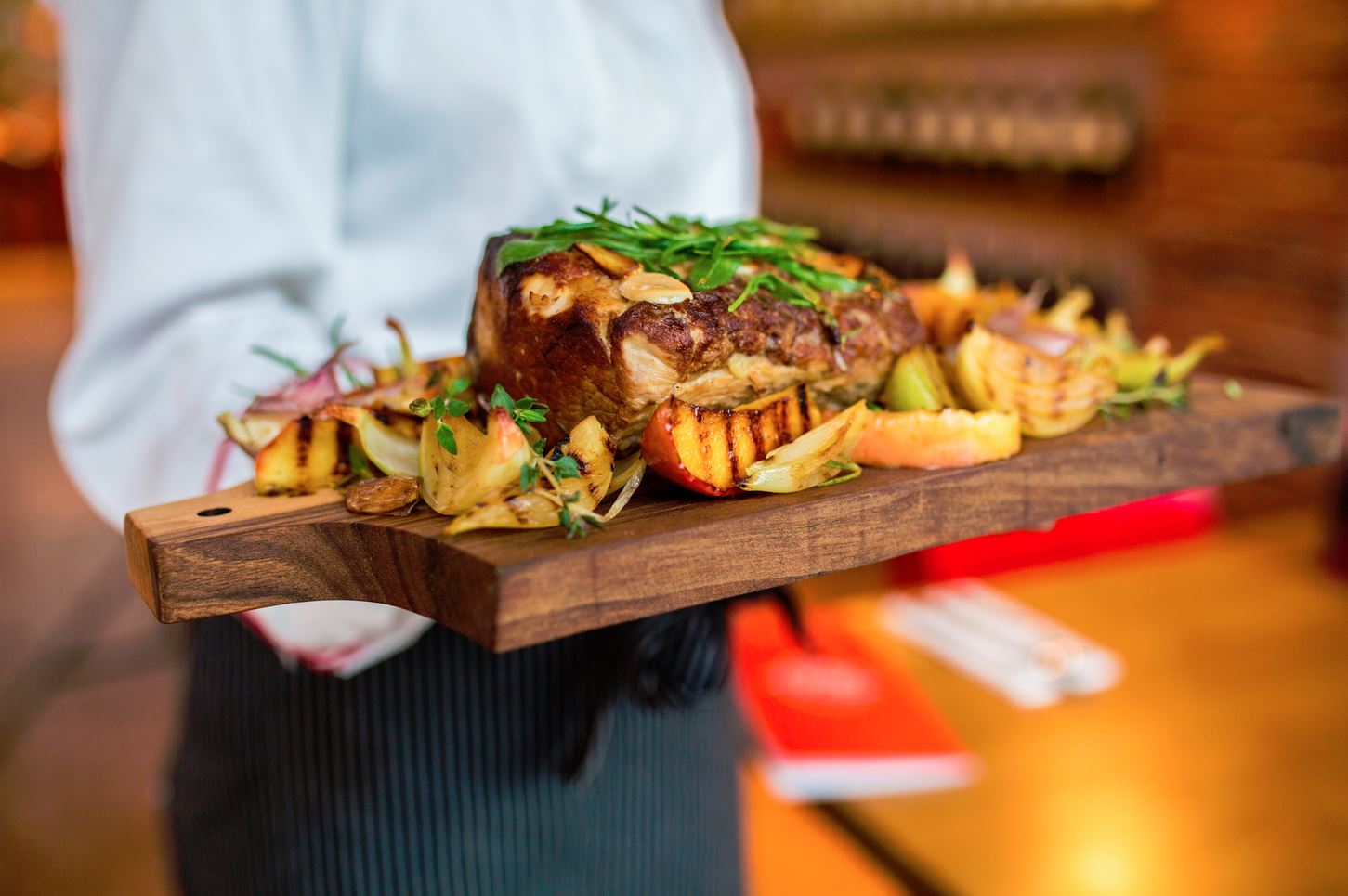 A chef holding a wooden board with meat and vegetables on it